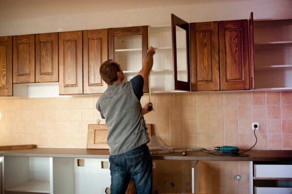 A contractor measuring and installing kitchen cabinets in a home.